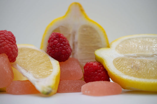 Fresh raspberries and lemon slices with colorful gummies on a white background, illustrating vibrant flavors.