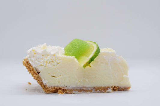 Slice of creamy lime pie topped with whipped cream and lime slice on graham cracker crust.