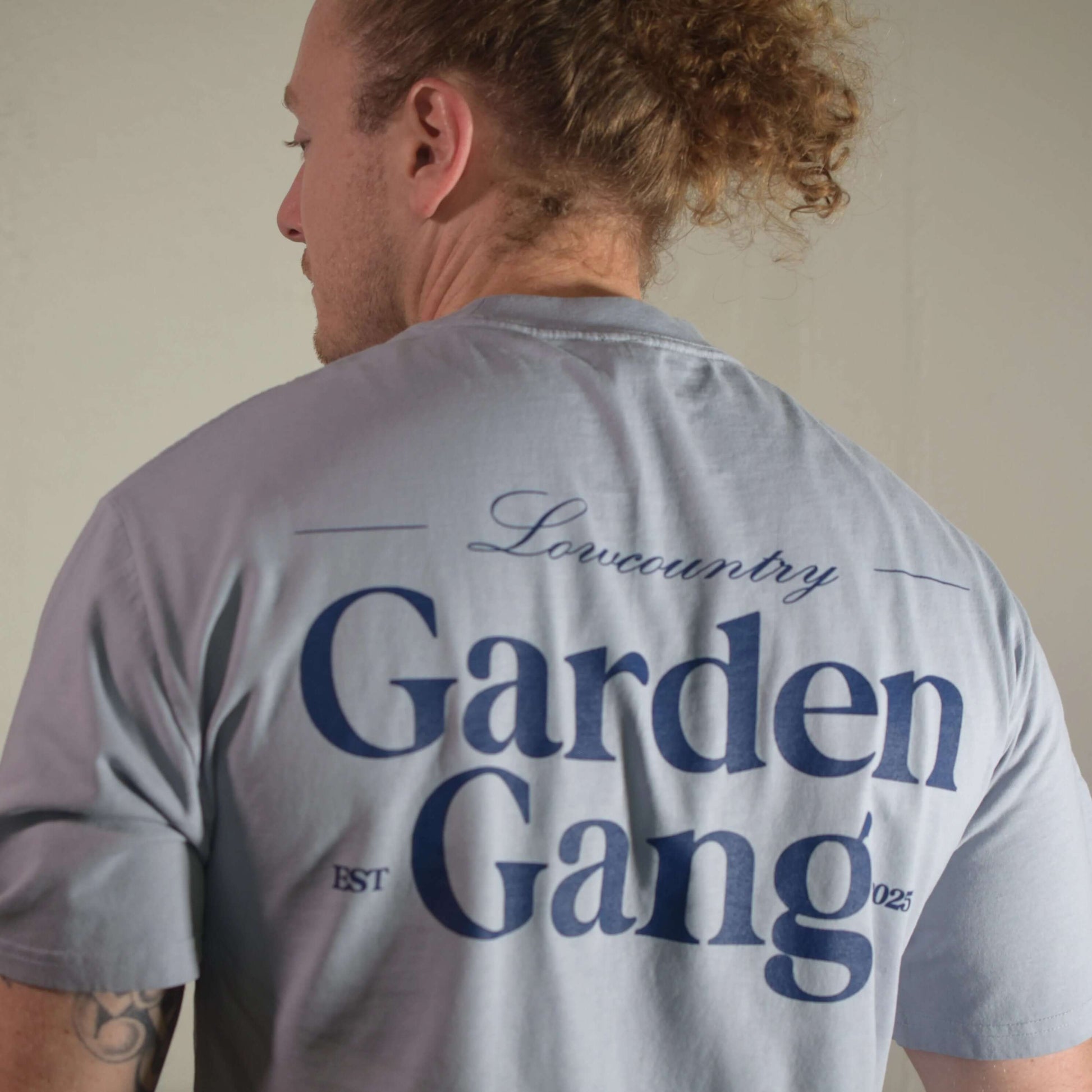 Back view of a man wearing a Lowcountry Garden Gang Tee Shirt with stylish typography.